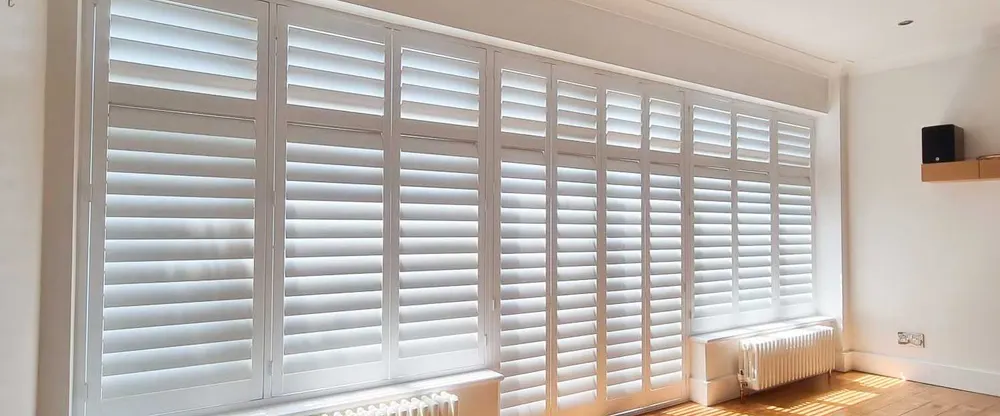 Long wall of windows in a bright room, lined with white full height shutters