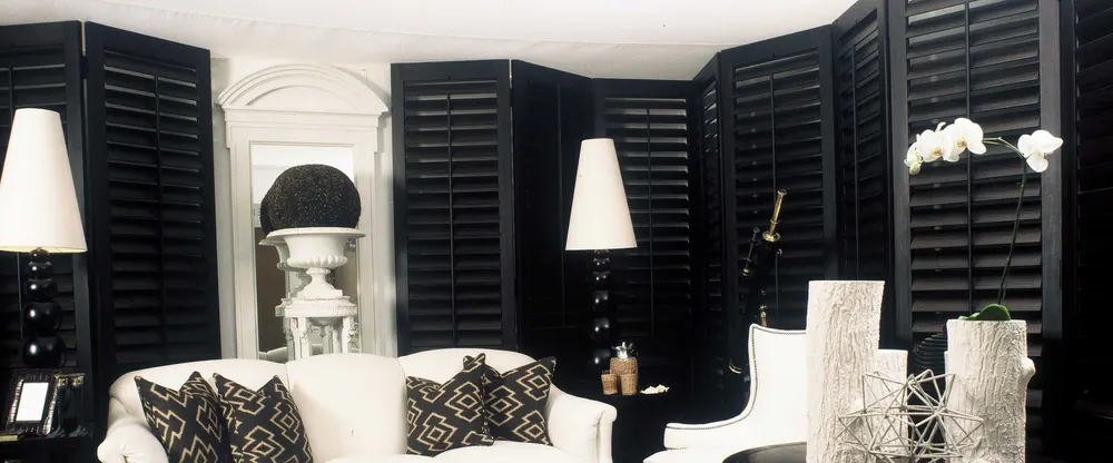 A white living room with black plantation shutters, louvres tilted part open