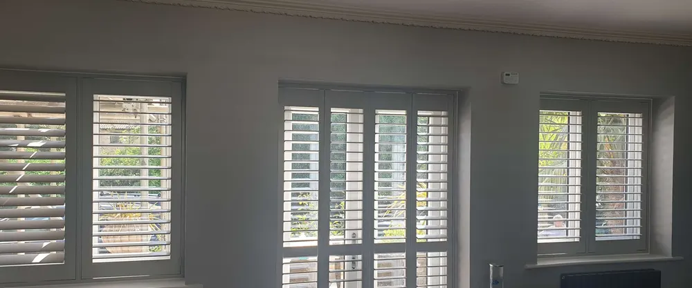 Living room with white shutters on two windows and a taller set between them