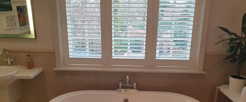 White shutters on a bathroom window above a freestanding bath