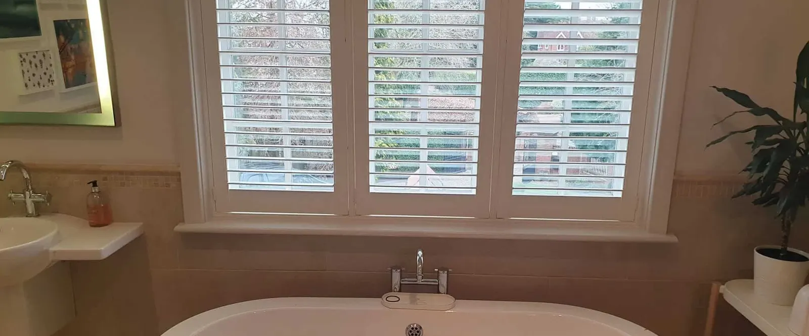 Roll-top bath beneath a bathroom window with white shutters