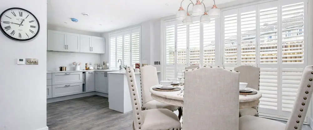 Kitchen diner with white full height shutters on the windows behind the table