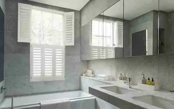 Stone-walled bathroom with white tier-on-tier shutters over the bath
