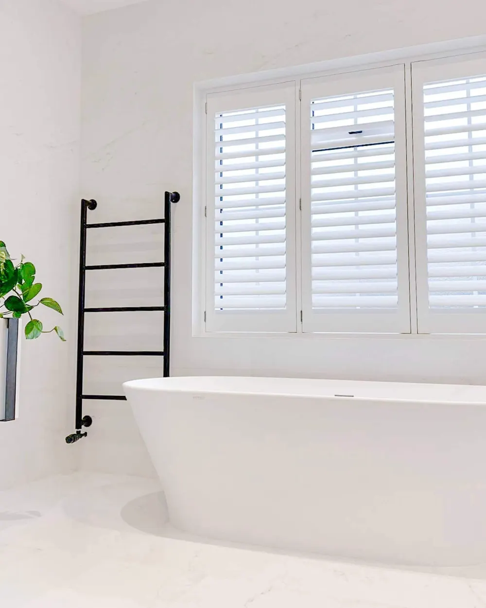 Freestanding bath under a window fitted with white Hollywood shutters