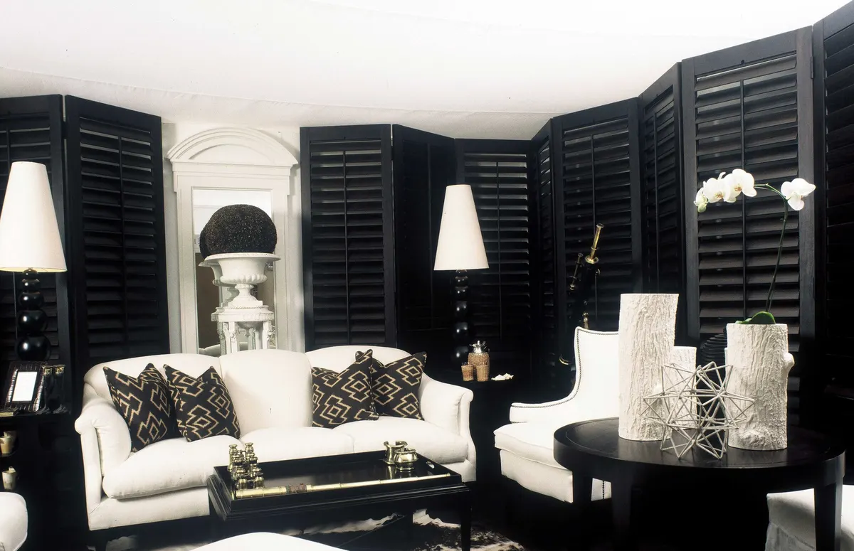 Living room with white sofas surrounded by black louvred shutters