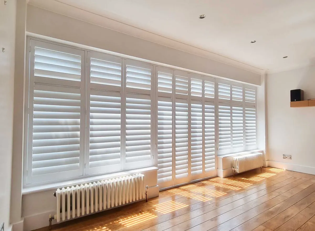 Full-height white shutters running the length of a sunny living room