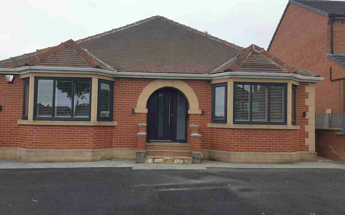 Brick bungalow seen from the front, its angled bay windows fitted with shutters