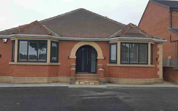 Brick bungalow seen from the front, its angled bay windows fitted with shutters