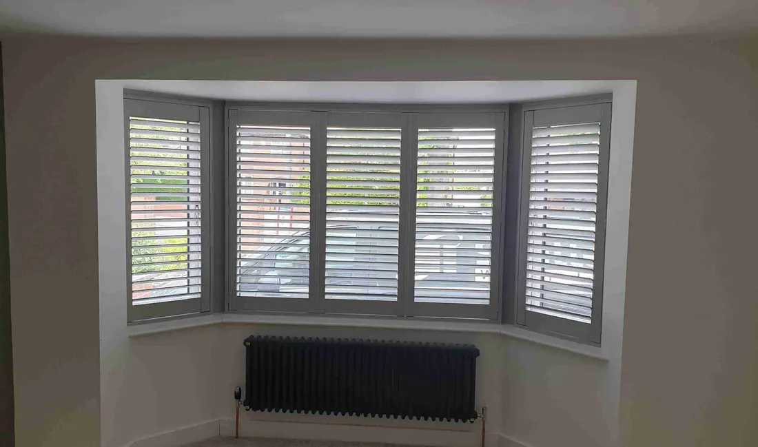Black radiator below white shutters in an angled bay