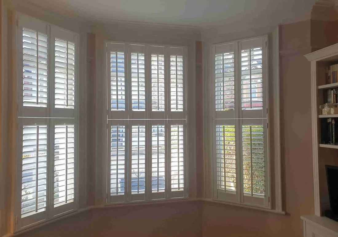 Bookcase next to an angled bay of full height shutters