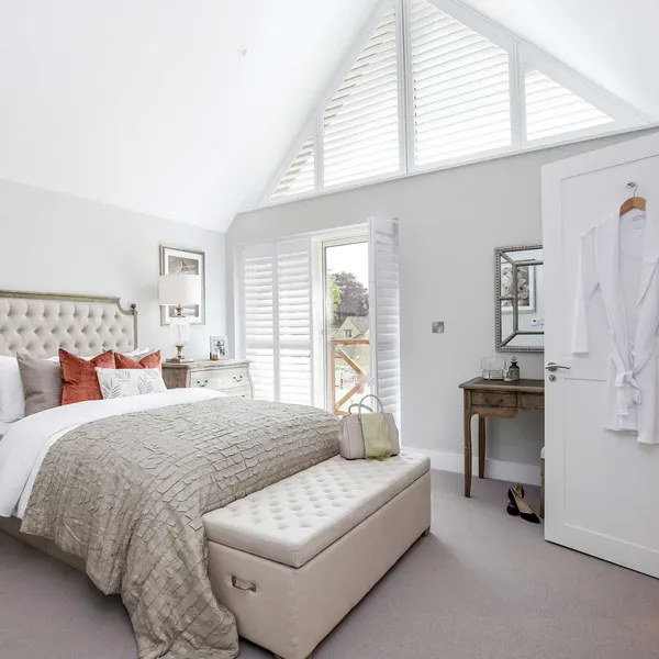 Tufted bed in a bright gable bedroom with angled shutters
