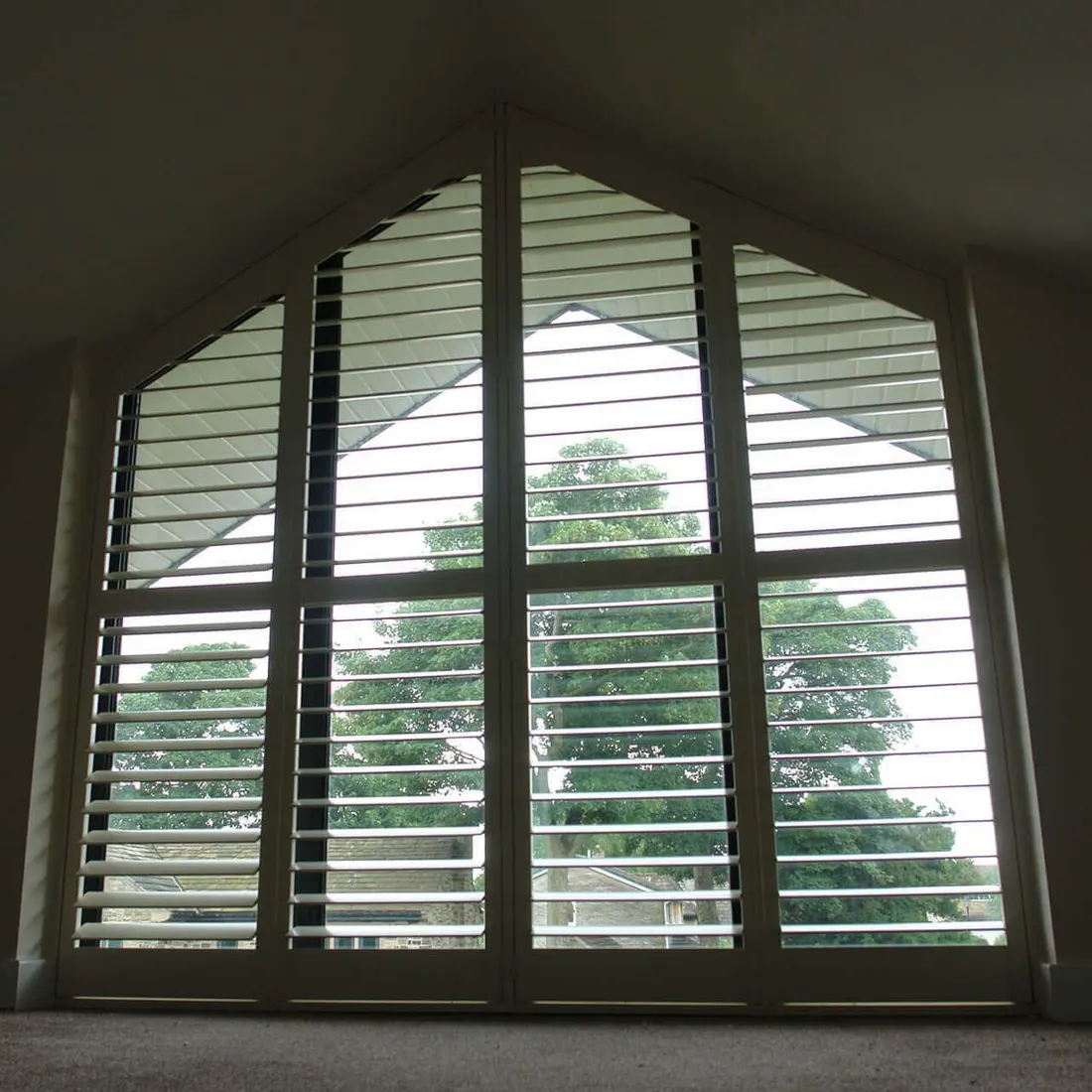 A tall gable window with grey shutters and angled panels across the top