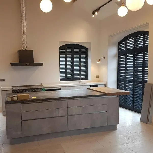 Kitchen island in front of tall arched windows with dark shutters