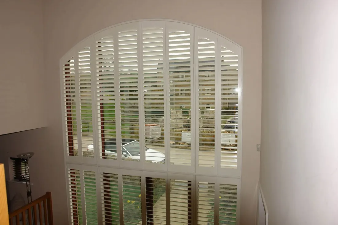 Tall window with white shutters and a shaped panel filling the arch