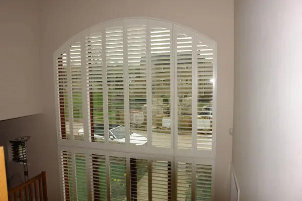 A tall window with white shutters and an arch-shaped panel filling its top