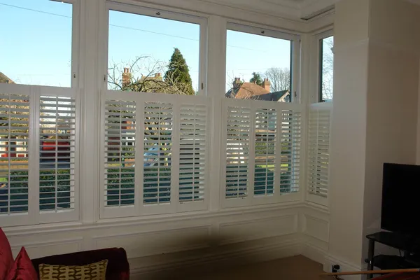 Wide living room window, its lower half covered by white café style shutters