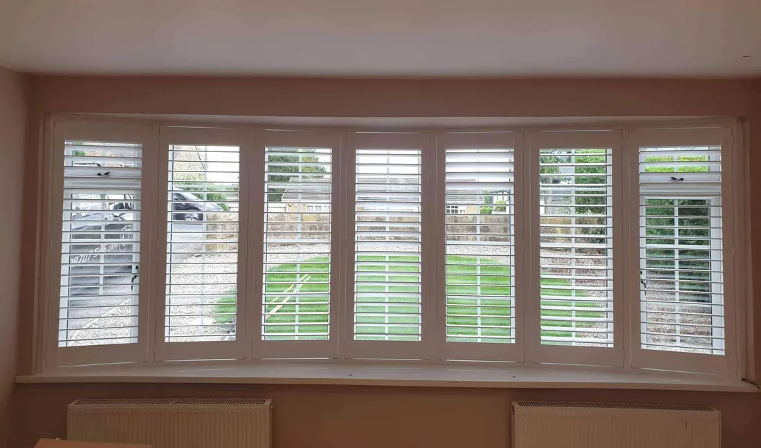 Garden lawn seen through the open louvres of curved bay shutters