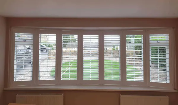 Garden lawn seen through the open louvres of curved bay shutters