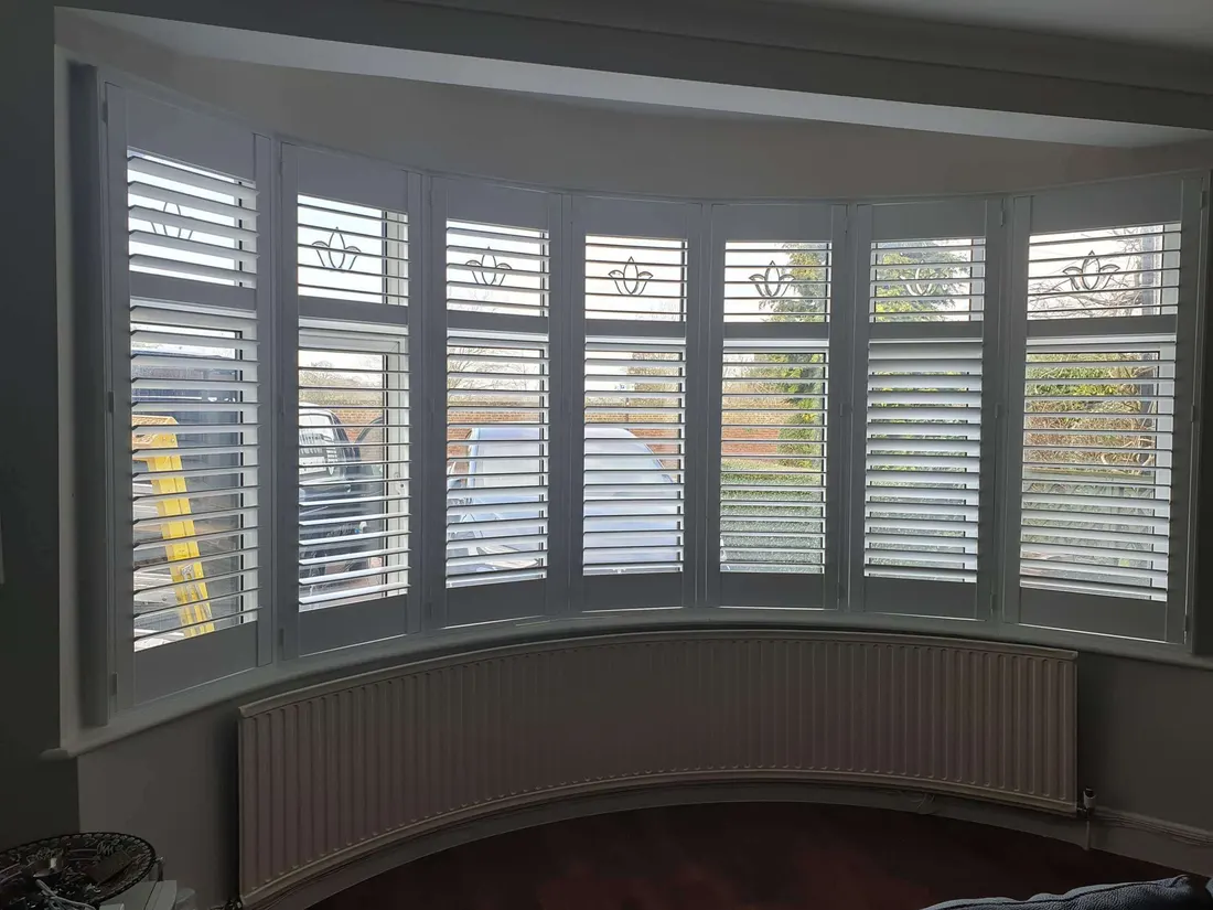 Seven windows round a curved bay, each fitted with a white shutter