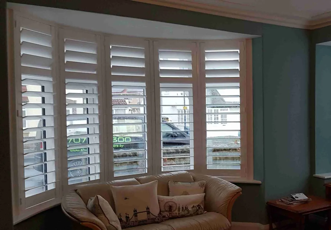 Cream sofa and cushions in front of curved bay shutters