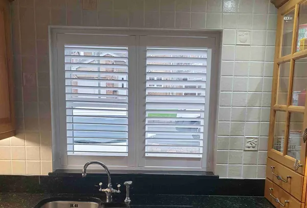 Kitchen sink below a tiled window fitted with white full height shutters