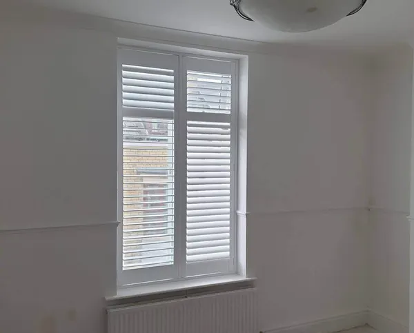 Sash window dressed in white full height shutters, with a radiator underneath