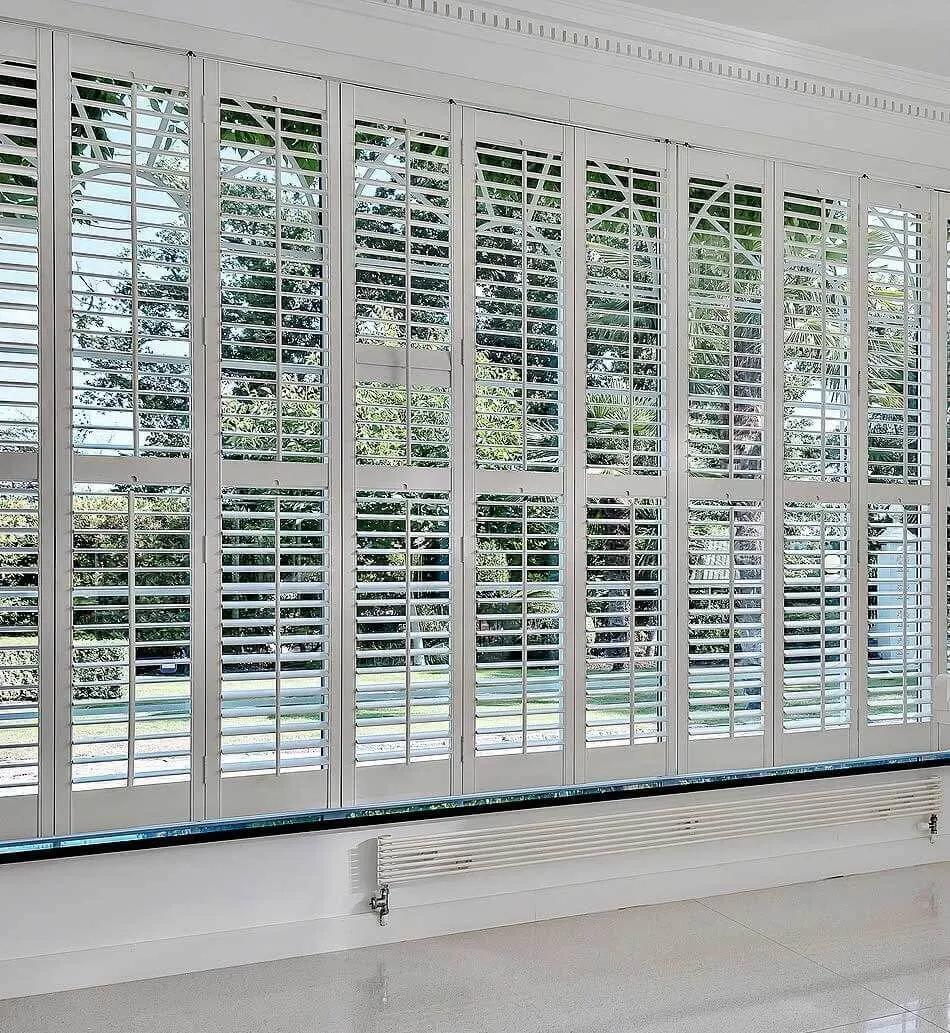 Louvres tilted open along a long run of white full height shutters facing the garden