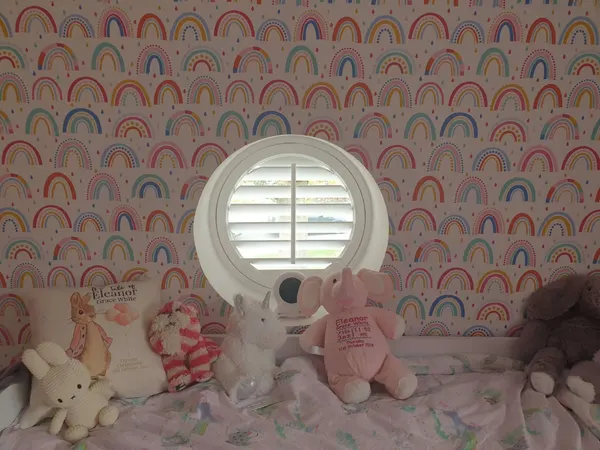 Rainbow wallpaper round a child's room window with a round shutter