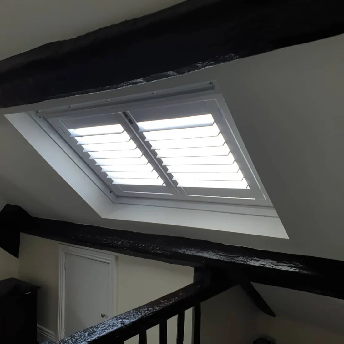 Loft landing with dark beams and white shutters on the skylight