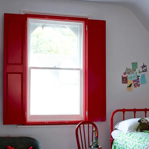 Red solid panel shutters folded open either side of a white bedroom window