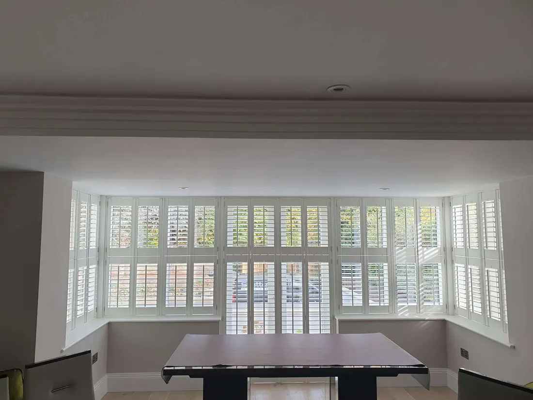 Dining room with a wide square bay lined with white full height shutters