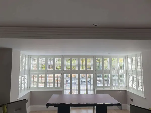 Dining room with a wide square bay lined with white full height shutters