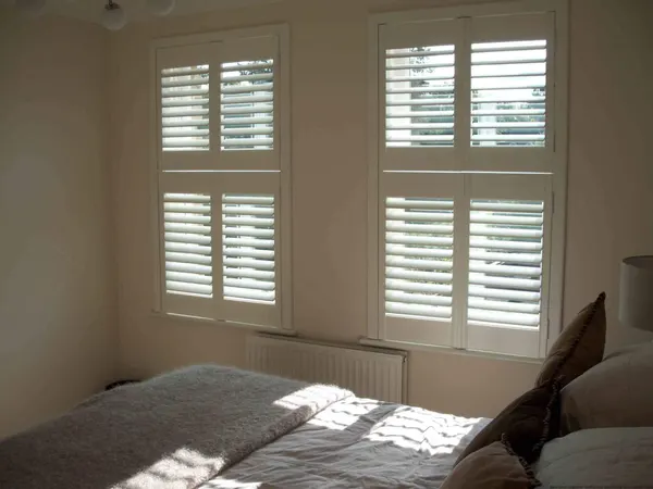 Sunlight falling across a bed from a window with white tier-on-tier shutters