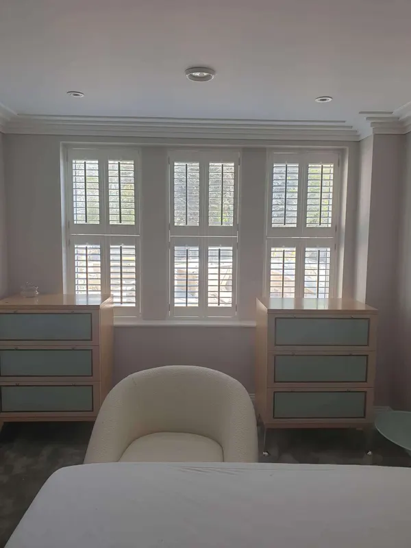 Two chests of drawers under a wide bedroom window with white tier-on-tier shutters